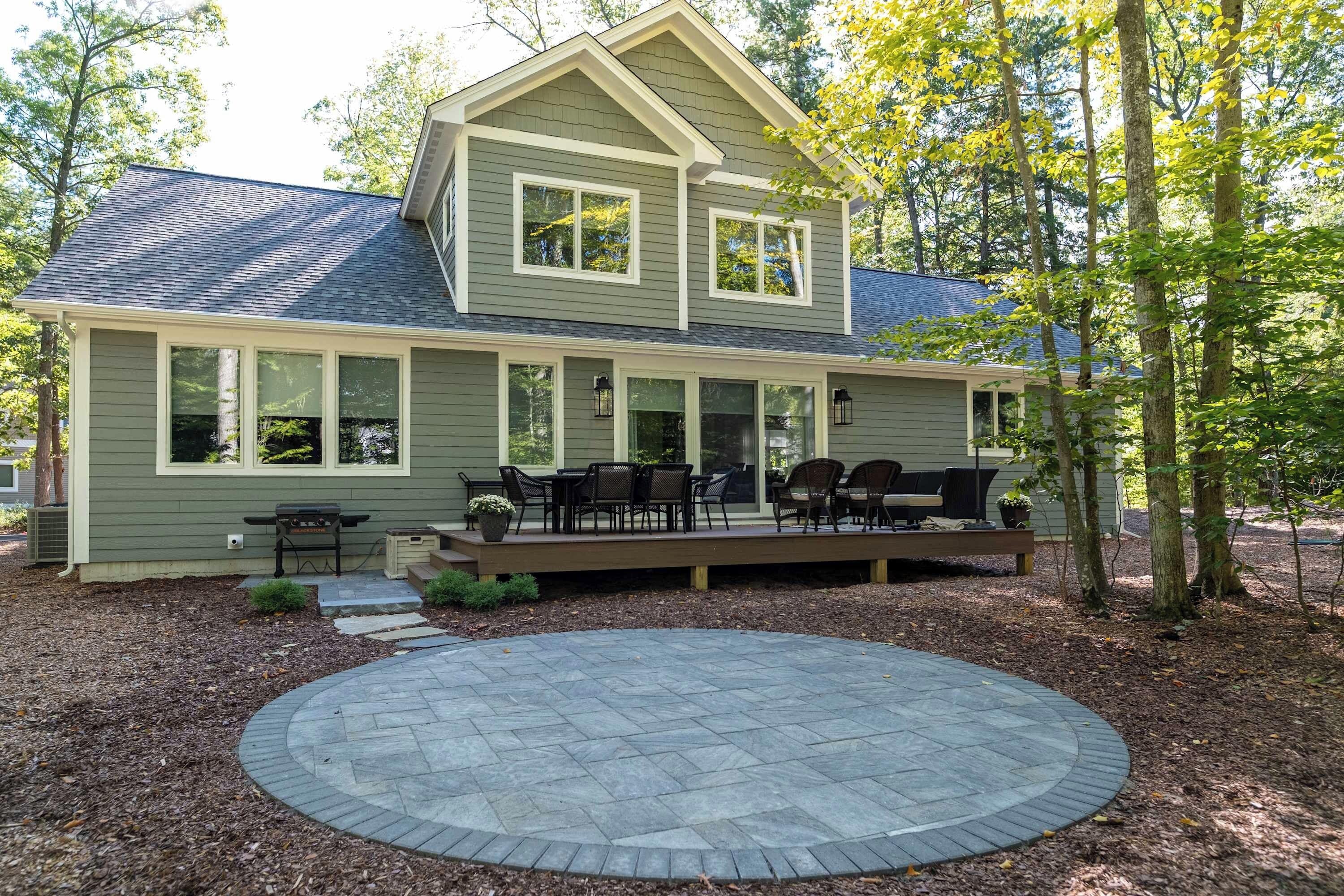 A two-story house with a covered patio and a circular stone patio in front.