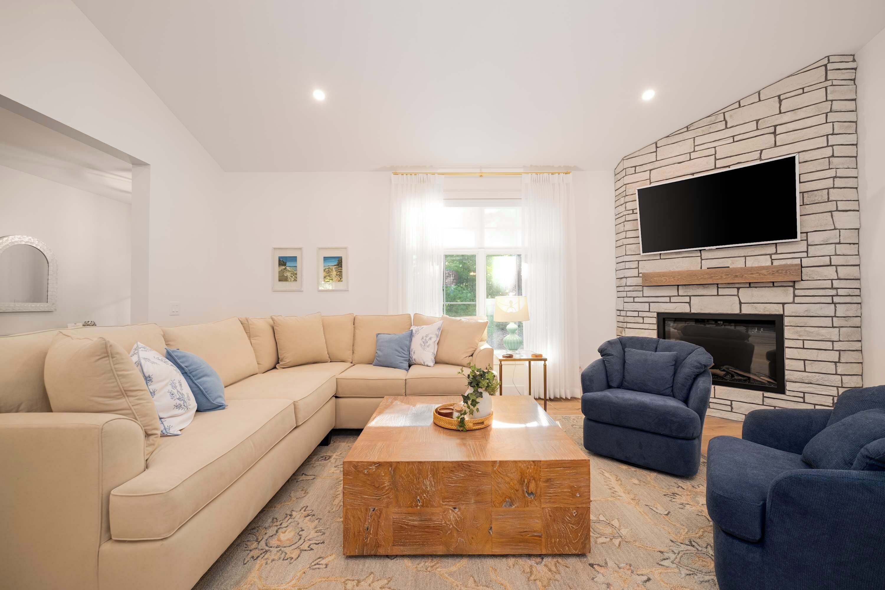 Una sala de estar con un sofá seccional color beige, un sillón azul, una mesa de centro de madera y una chimenea de piedra.