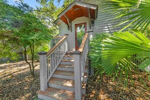 A house with a wooden staircase leading to a front door, surrounded by trees and a fence. - Kiawah Exclusives | 447 Oceanwoods Cottage (Kiawah Island)