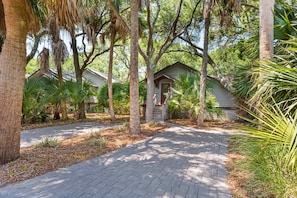 A pathway leading to a row of small, single-story cabins surrounded by trees. - Kiawah Exclusives | 447 Oceanwoods Cottage (Kiawah Island)