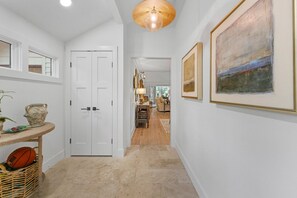 A hallway with a white door, a wicker basket with a basketball, and a painting on the wall. - Kiawah Exclusives | 447 Oceanwoods Cottage (Kiawah Island)