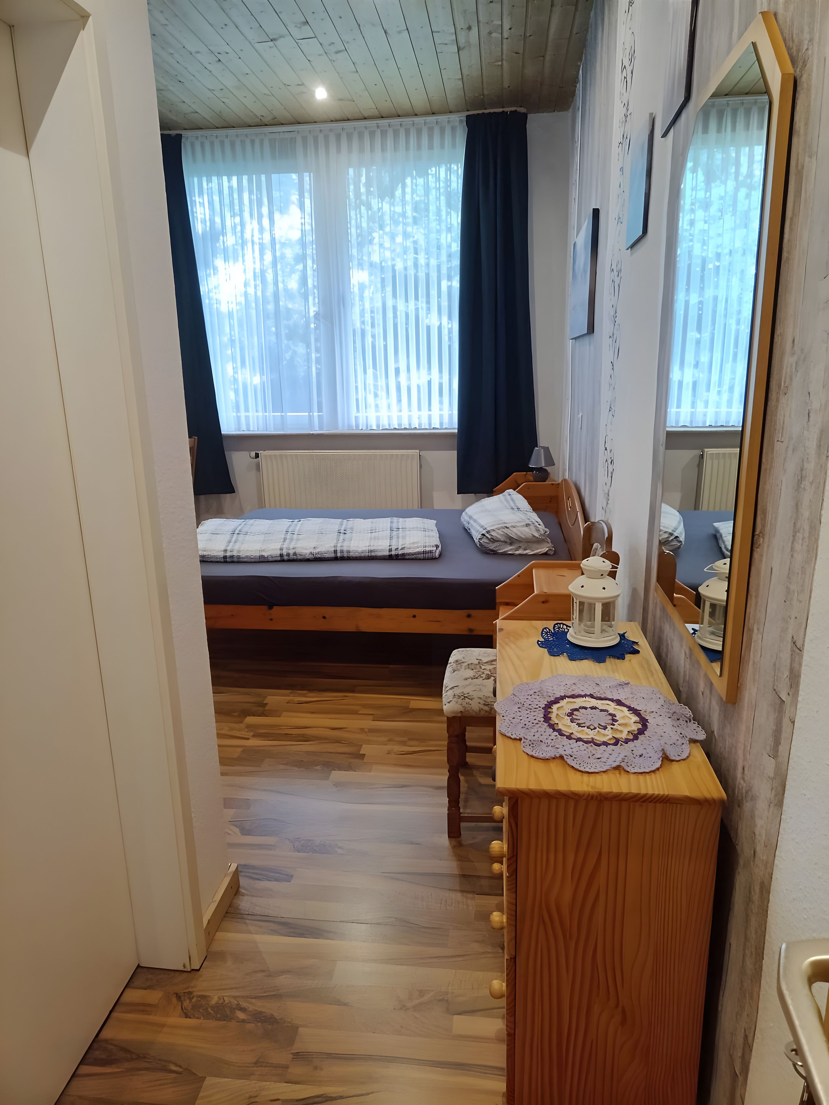 Ein Schlafzimmer mit einem Bett, einem Holzschrank, einem Spiegel und einem Fenster mit Vorhängen.