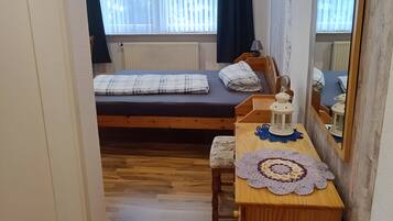 Ein Schlafzimmer mit einem Bett, einem Holzschrank, einem Spiegel und einem Fenster mit Vorhängen.