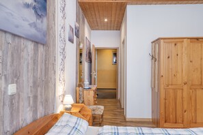 A wooden interior with a bed, a nightstand, a lamp, a mirror, and a wardrobe.