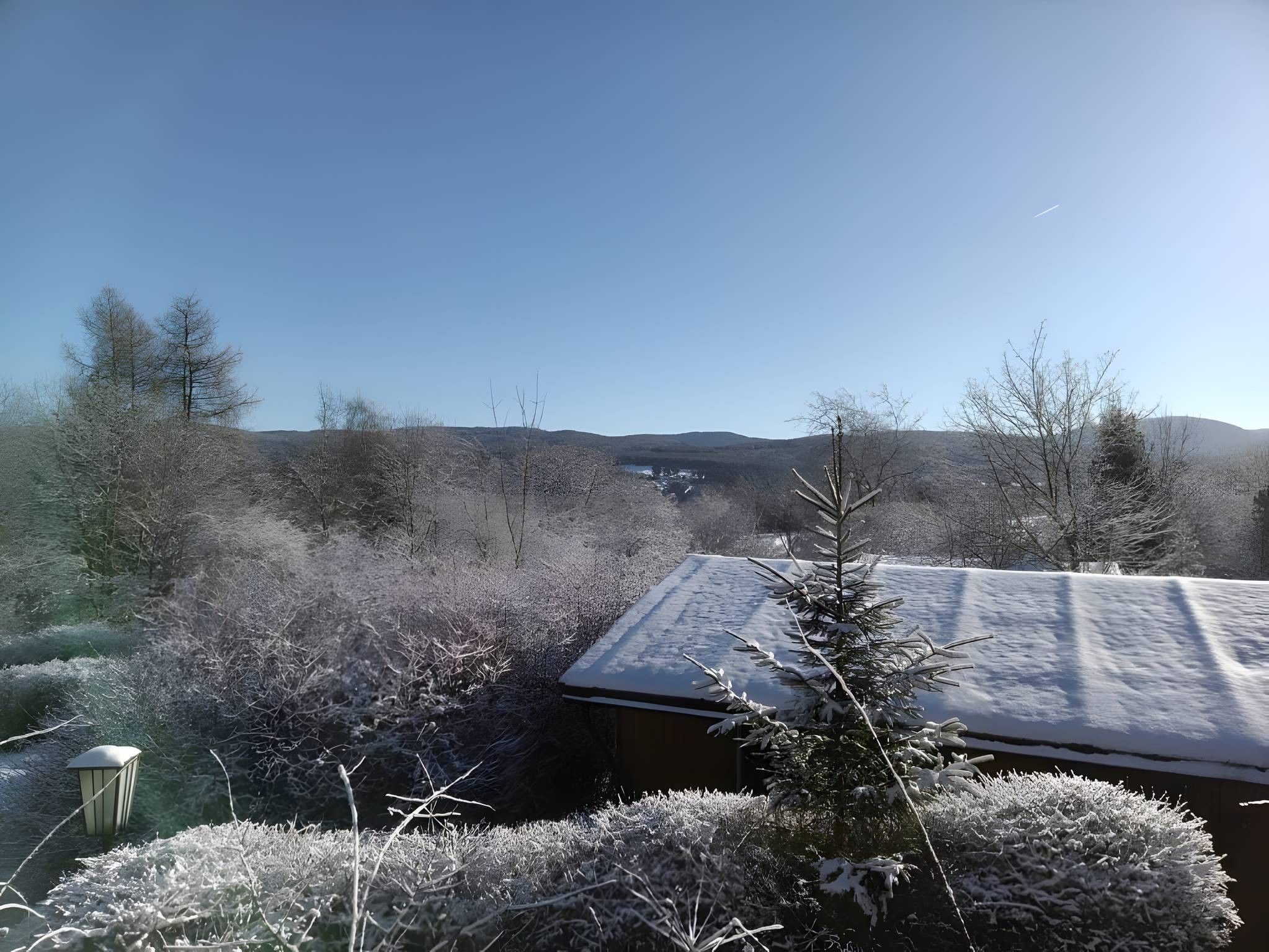 Une maison dont le toit est recouvert de neige, entourée d’une végétation givrée et sous un ciel dégagé.