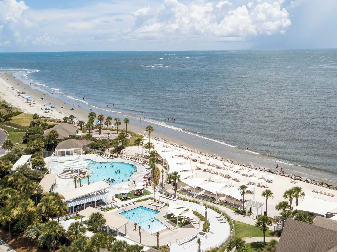 Un resort con una amplia zona de piscina, acceso a la playa y palmeras.