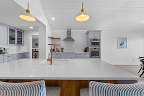 A modern kitchen with a large island, stainless steel appliances, and pendant lighting. - Seabrook Exclusives | 1354 Pelican Watch (Seabrook Island)