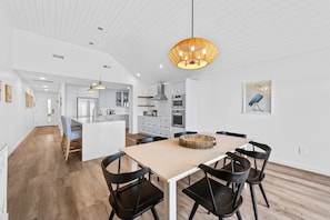 A modern kitchen with white cabinets, a central island, and a dining area with a wooden table and black chairs. - Seabrook Exclusives | 1354 Pelican Watch (Seabrook Island)