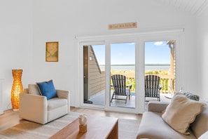 A room with a sofa, a chair, a table, and a view of the beach through a sliding door. - Seabrook Exclusives | 1354 Pelican Watch (Seabrook Island)