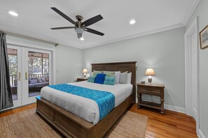A bedroom with a wooden bed, a ceiling fan, a nightstand, and a view of the outdoors through a glass door. - Seabrook Exclusives | 1151 Summerwind (Seabrook Island)