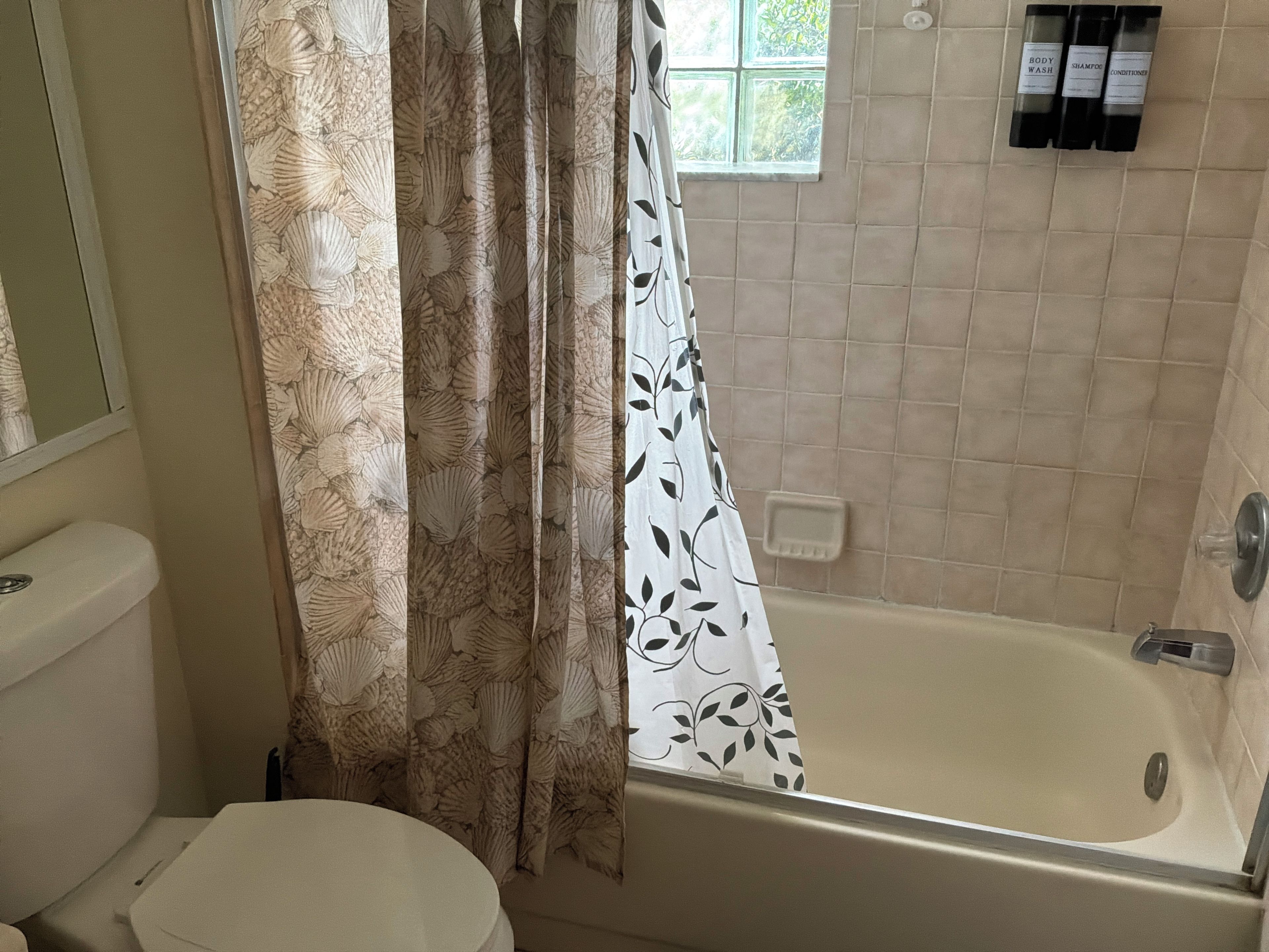 A bathroom with a toilet, a bathtub, and a shower curtain with a leaf pattern.