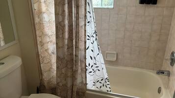 A bathroom with a toilet, a bathtub, and a shower curtain with a leaf pattern.