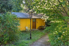 Eine gelbe Holzhütte mit Tür, einer kleinen Veranda und einem Tisch mit Stühlen.