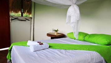 A bed with a white and green bedspread, a white canopy, and a small bedside table with a plant.