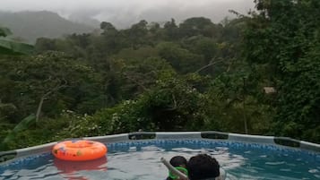 A circular swimming pool with a person and a child inside, surrounded by lush greenery.