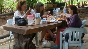 A group of people seated at a wooden table outdoors with a natural backdrop.