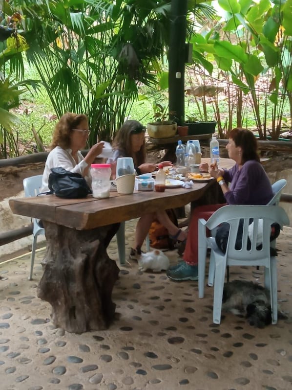 Un grupo de personas sentadas a una mesa de madera al aire libre, con un paisaje natural de fondo.