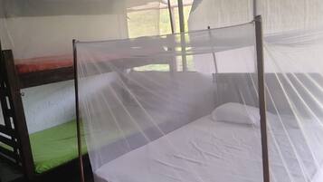 Una habitación con una cama bajo una mosquitera, una litera a la izquierda y una ventana con vistas a follaje.