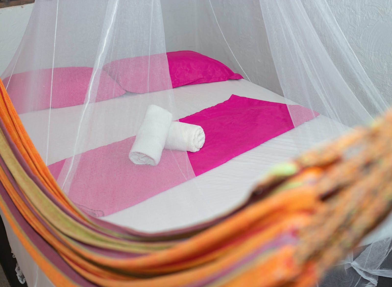A bed with a mosquito net, a pink pillow, and a rolled white towel.