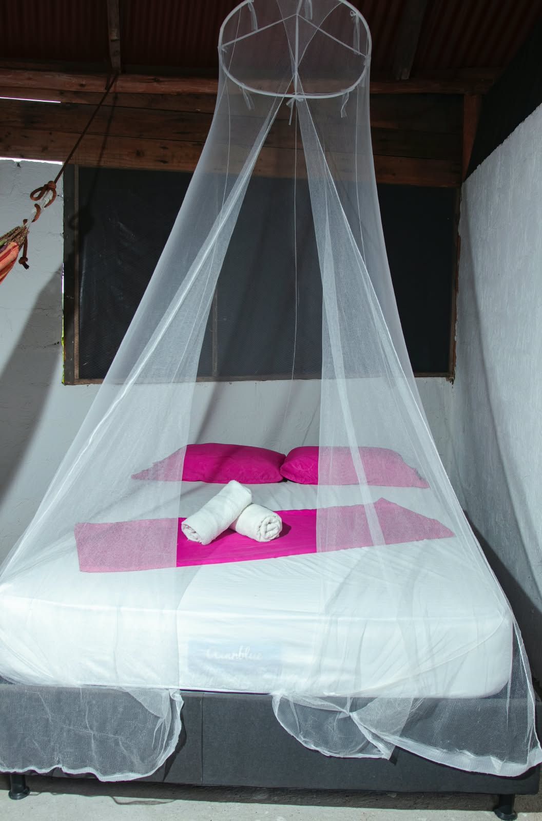 A bed with a mosquito net, pink pillows, and rolled towels.