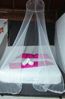Una cama con mosquitero, almohadas rosas y toallas enrolladas.