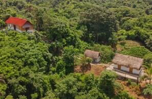 Un paisaje rural con tres casas de techo de paja rodeadas de abundante vegetación.