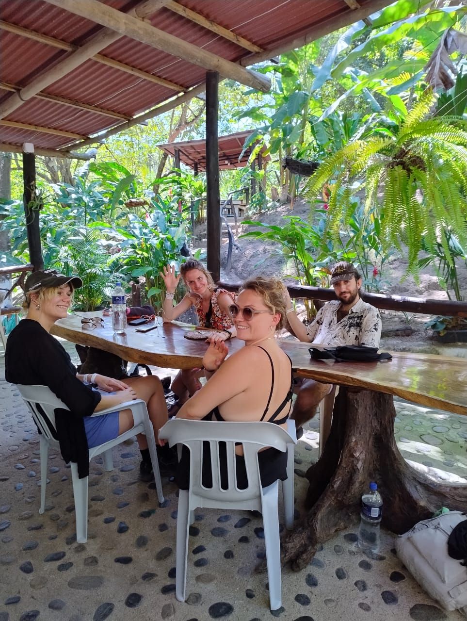 A group of people seated at a round table outdoors with a natural backdrop.