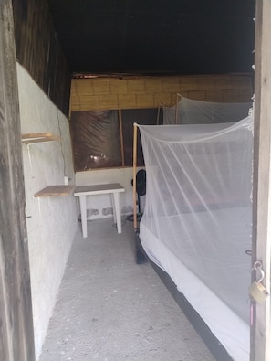 A small, enclosed room with a single bed, a bench, and a table.