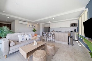 Una sala de estar moderna con un sofá, una mesa de centro y una zona de cocina con barra y electrodomésticos.