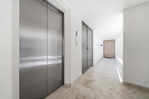 A corridor with a modern elevator, a wooden door, and a clean floor. - Brand New Pet-friendly Condo - Private Pool (Cabo San Lucas)