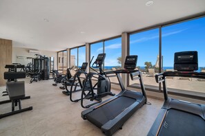 A gym with treadmills, elliptical machines, and weight equipment, overlooking a clear sky and distant landscape. - Brand New Pet-friendly Condo - Private Pool (Cabo San Lucas)