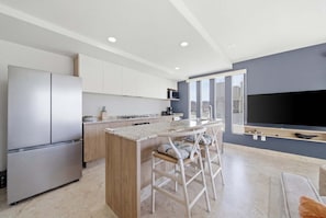 Una cocina moderna con una isla central, electrodomésticos de acero inoxidable y un televisor grande montado en la pared.