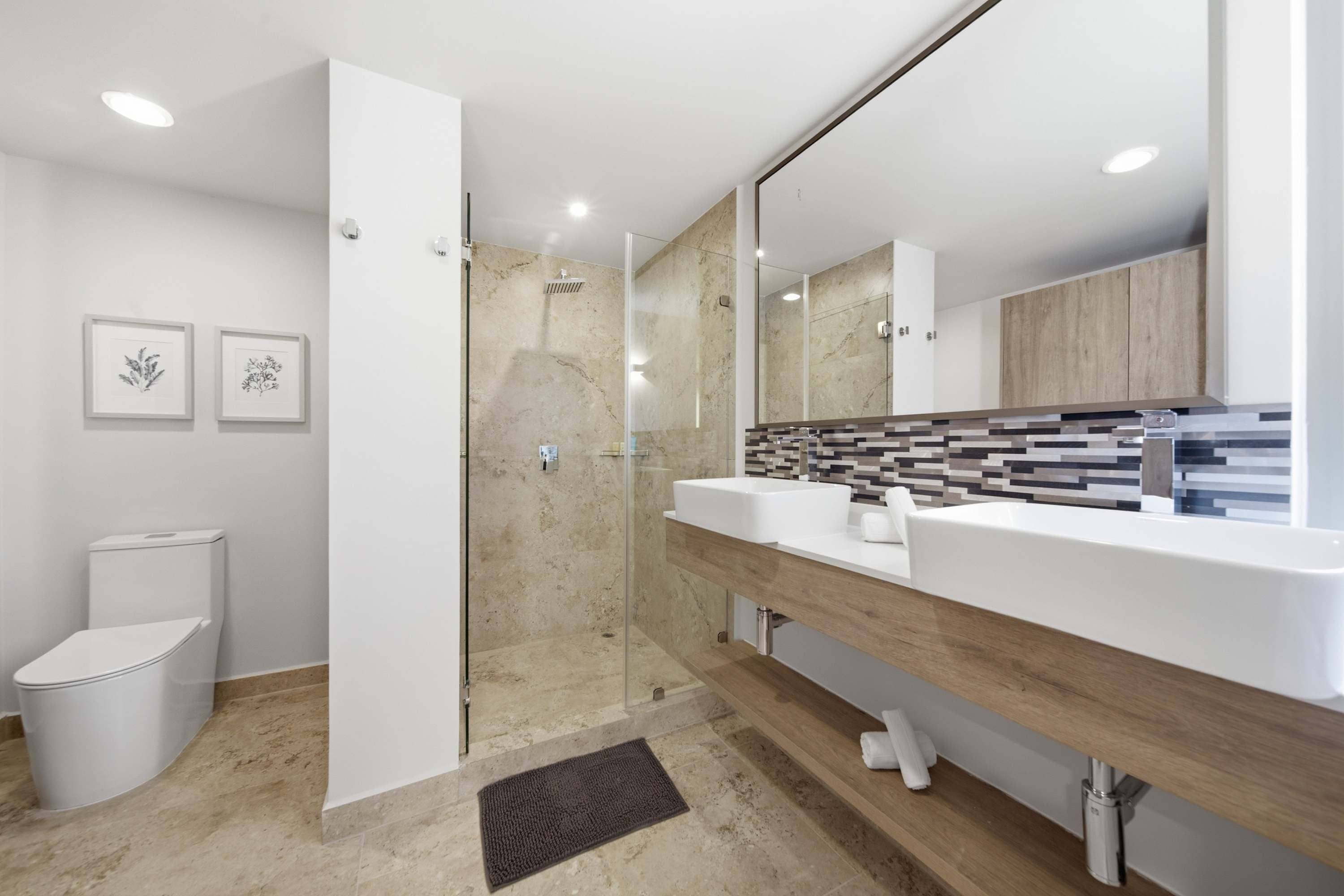 A modern bathroom with a glass-enclosed shower, a white toilet, and a vanity with a tiled backsplash.