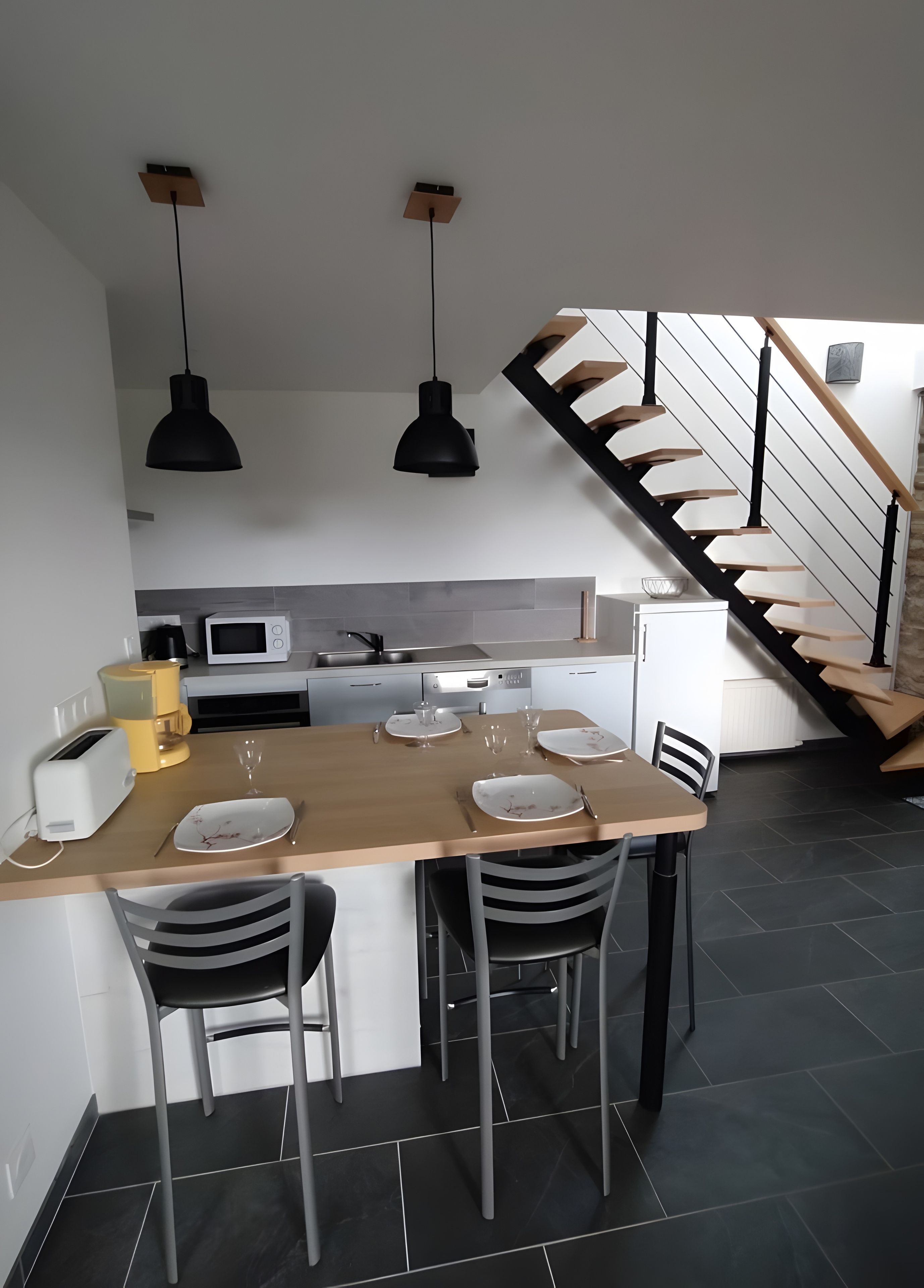 A modern kitchen with a dining area, a staircase, and a view of the living room.