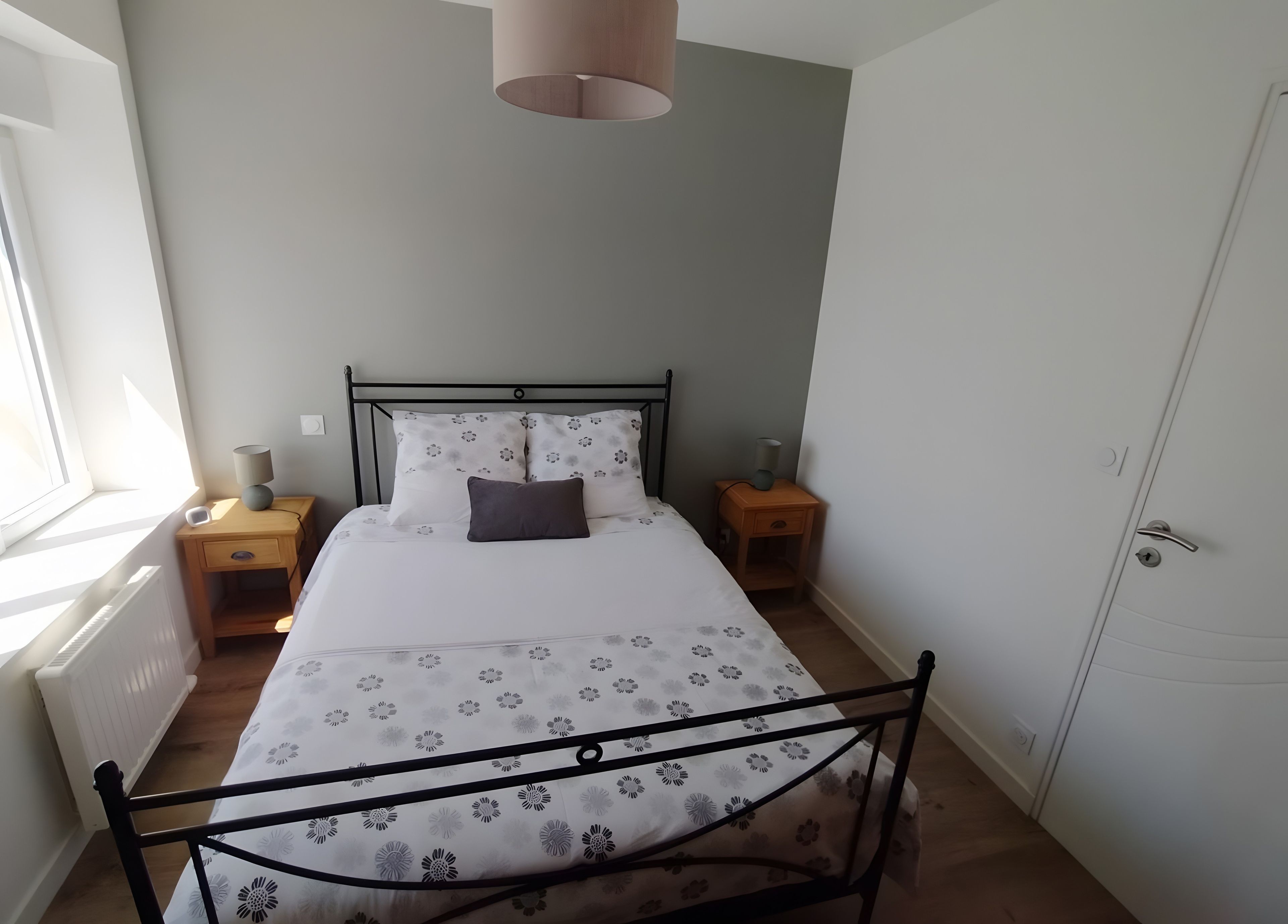 Un dormitorio con cama, mesitas de noche, una ventana y una puerta.