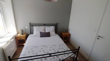 Un dormitorio con cama, mesitas de noche, una ventana y una puerta.