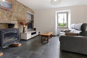 A modern living room with a stone wall, a fireplace, a sofa, and a television.