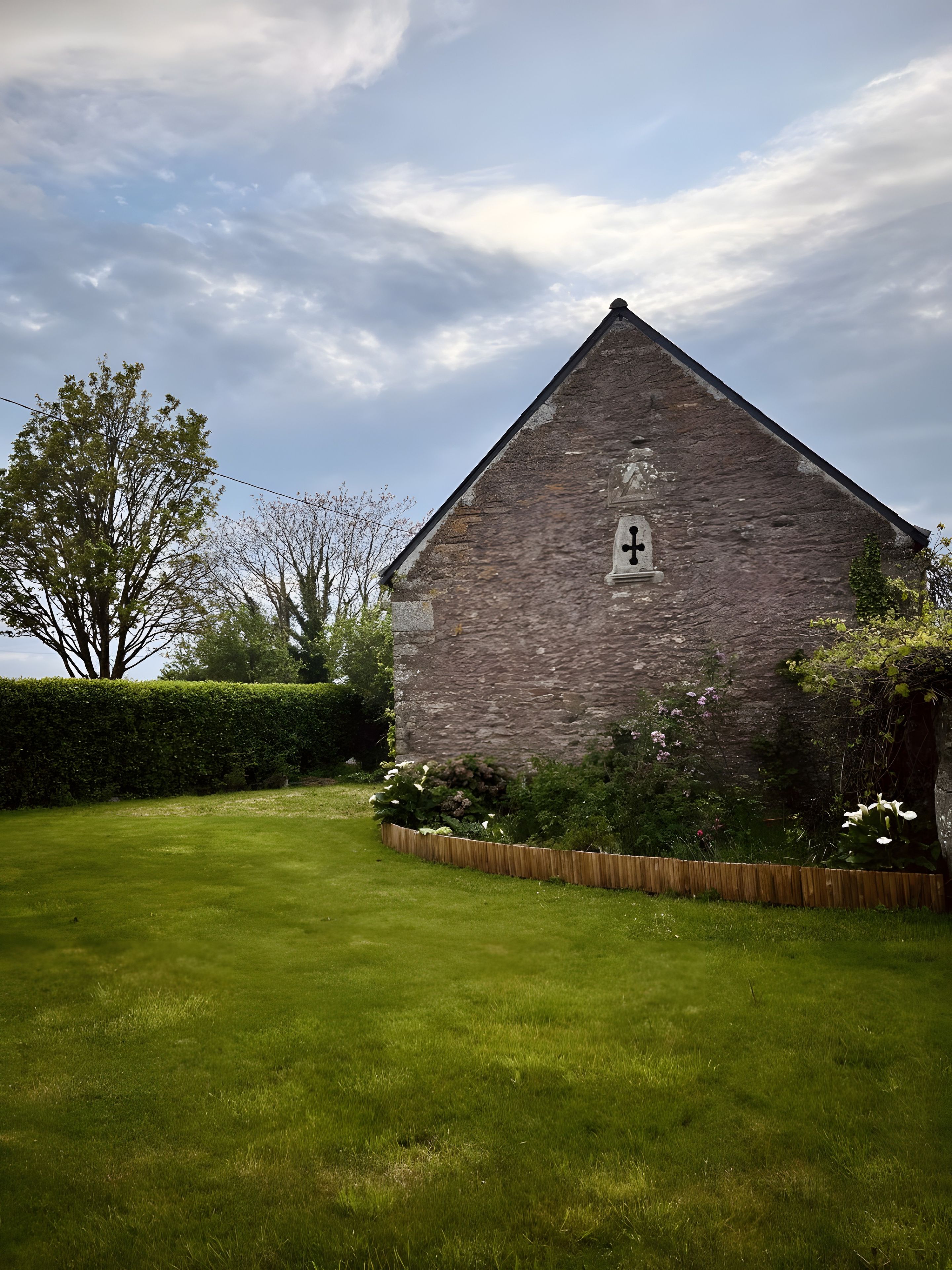 A stone building with a small window, surrounded by a well-maintained lawn and a hedge.