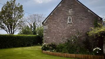 A stone building with a small window, surrounded by a well-maintained lawn and a hedge.