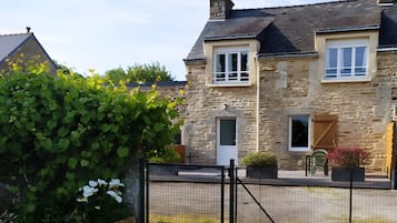 A stone house with a fenced yard, a wooden gate, and a small garden area.