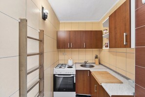 A compact kitchen with wooden cabinets, a stove, an oven, a sink, and a countertop with a cutting board.