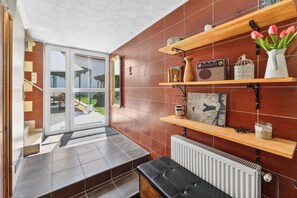 A modern interior with a sliding glass door leading to an outdoor area, wooden shelves with various items, and a black leather bench.