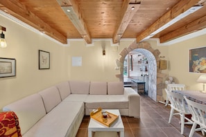 A modern living room with a sectional sofa, a dining table with chairs, and a kitchen visible through an archway.