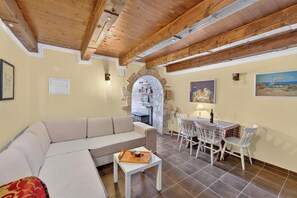 A living room with a beige sofa, a small table with a tray, and a dining area with a table and chairs. - Traditional Stone House Near St. James Church, Private Yard (Međugorje)