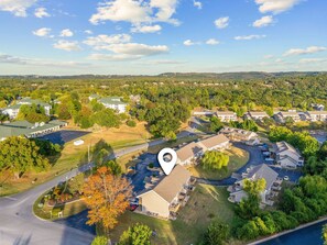 An aerial view of a residential area with multiple houses, a central road, and a large building with a parking lot. - Fall Creek Condo | Minutes to Strip, SDC & Lakes (Branson)