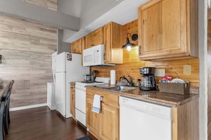 A kitchen with wooden cabinets, a white refrigerator, a microwave, a coffee maker, and a dishwasher. - Fall Creek Condo | Minutes to Strip, SDC & Lakes (Branson)