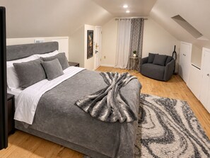 Un dormitorio con cama, sofá gris, alfombra estampada y una puerta con cortinas.