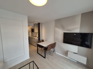 Ein modernes Apartment mit Essbereich, einer Küche und einem großen, an der Wand montierten Fernseher.