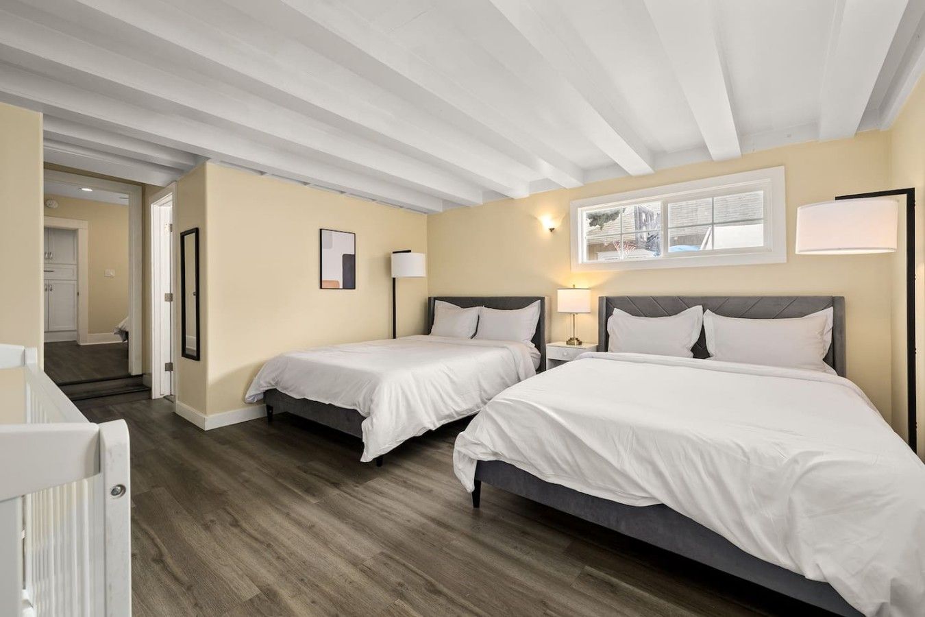Een hotelkamer met twee bedden, een houten vloer, een wit plafond en een raam met uitzicht.