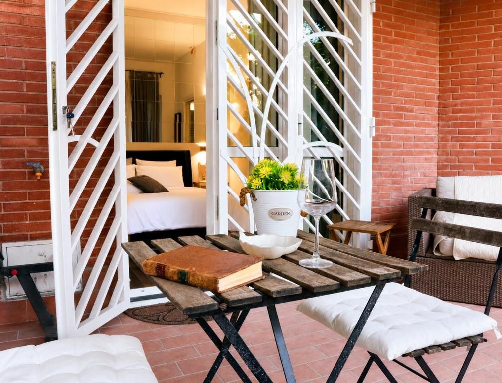 Un espace de détente extérieur accueillant, avec une table en bois, une chaise en osier et un banc blanc doté de coussins.
